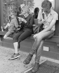 Parents looking at cell phones on Sheridan Square near Stabrucks in Greenwich Village with young boy.